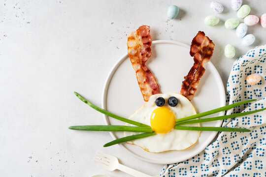 Easter concept with funny fried egg bunny and becon on plate on white background, top view