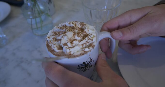 Person's hand setting down mug of hot chocolate with cream inside then picking it up - closeup
