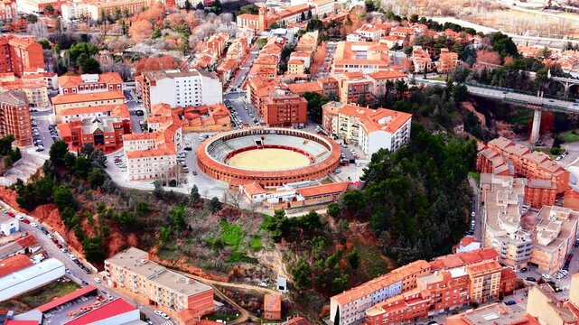 Elevated aerial view of a round bullring arena surrounded by trees and residential apartment buildings in an urban setting. Circular bullring in Spanish city.