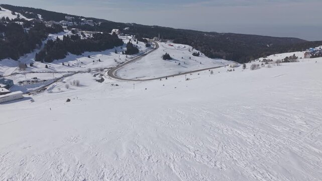 Aerial forward tracking shot over a snow-covered ski resort and mountain road at Uludag