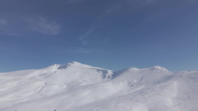 Aerial forward tracking shot flying towards the majestic snow-capped mountain peak of Uludag under a clear blue sky