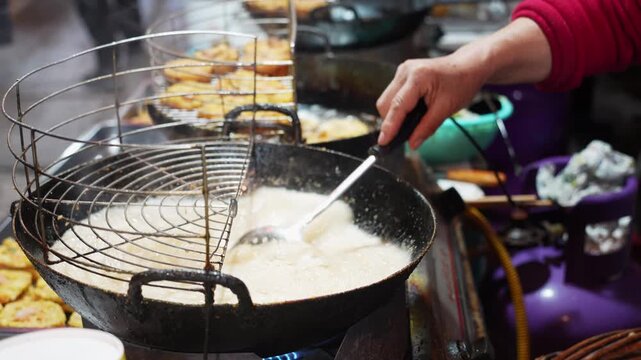 Street vendor deep frying snacks in bubbling hot oil at a night market
