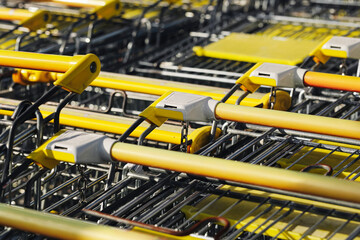 Shopping carts connected together in supermarket trolley line. Metal grocery carts with yellow handles stacked in row. Retail shopping equipment ready for customers in store.