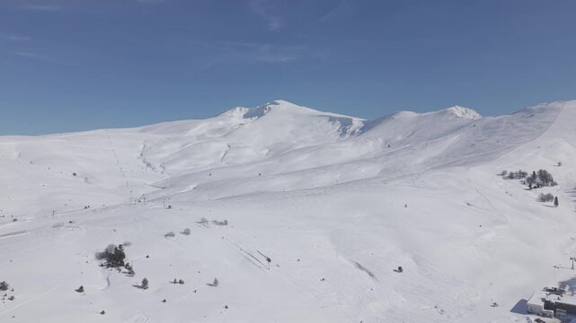 Aerial forward tracking shot flying towards the majestic snow-capped mountain peak of Uludag under a clear blue sky