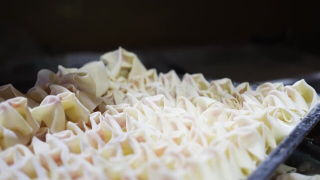 Handmade wontons being carefully arranged on a tray with detailed pleats and fresh dough