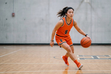 Fototapeta premium Athletic Asian woman demonstrates basketball pivot move in orange uniform