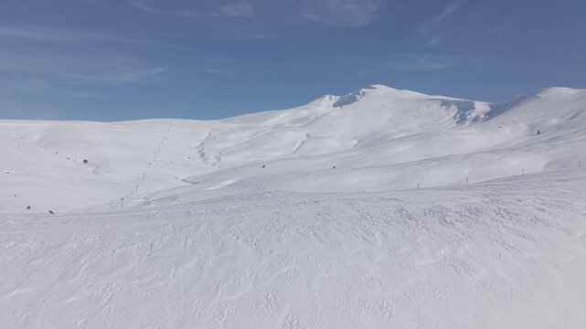 Aerial backward tracking shot pulling away from the snow-capped mountain peak of Uludag under a clear sky
