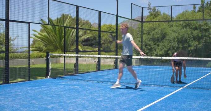 Diverse friends rallying on blue court with paddles, man stepping forward to reach short return