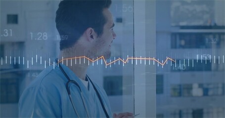 Standing doctor in blue scrubs with stethoscope in hospital looking out window with digital graph