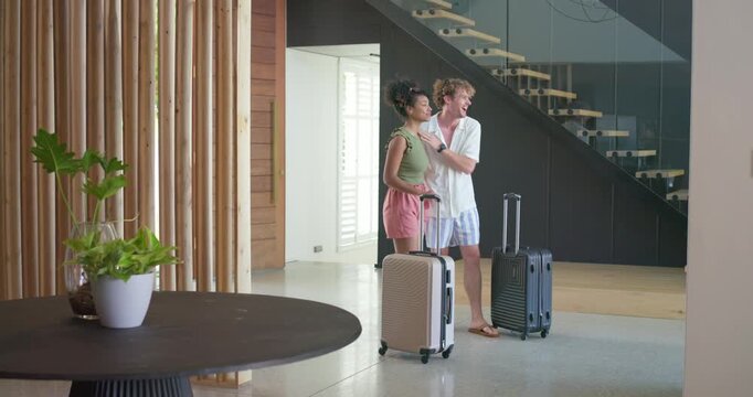 Couple in casual clothing arriving with luggage pausing in foyer pointing at stairs to decide