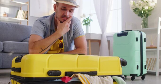 Man tourist looking and studying map before travelling, focused in smartphone screen and zooming place where he is going to rest, packing things in suitcases, preparing for good summer rest
