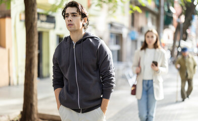 Upset young man walks away from her girlfriend on city street after argument or disagreement