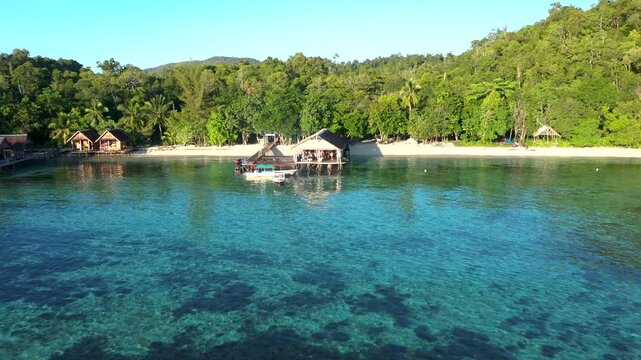 Golden hour aerial flyaway from jungle beach with jetty huts over water in Raja Ampat