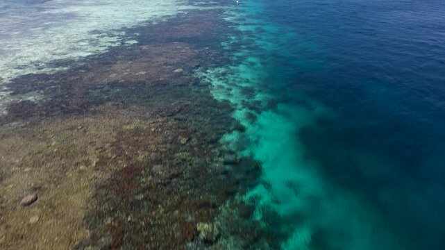 Aerial flyover of coral reef drop off into deep blue waters with island horizon in Raja Ampat Indonesia