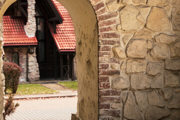 Obraz premium View through an old stone archway revealing a charming house with a red tiled roof