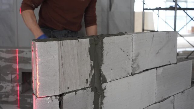 Worker wearing gloves laying aerated concrete blocks with laser level guidance