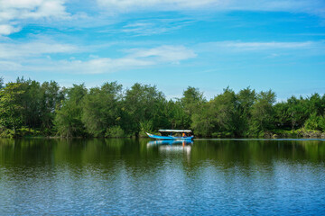 Obraz premium Small Blue Boat On Calm Lake With Tre Lined Shore And Blue Sky Reflections