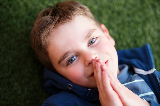 Overhead view of a young smiling boy lying on the grass praying