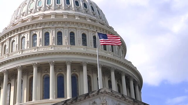 Capitol dome in Washington, D.C., with a flag waving. Close-up. Camera pans down.
