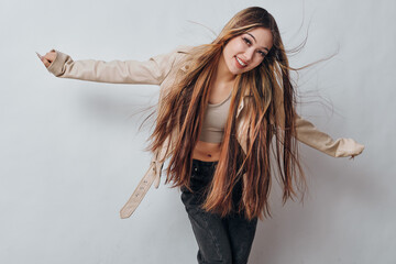 Young woman with long hair and casual clothes smiling and posing with open arms on gray background...