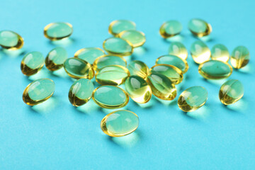 Pile of golden gelatin capsules on light blue background, closeup