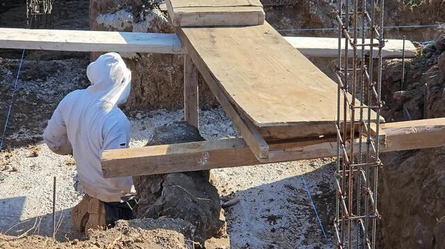 A bricklayer props up a wooden beam in an excavation trench