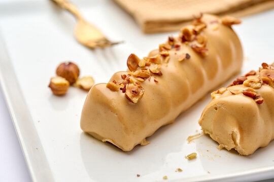Hazelnut mousse dessert bars with creamy gourmet caramel glaze, topped with chopped roasted nuts, presented on a white plate, ready for consumption