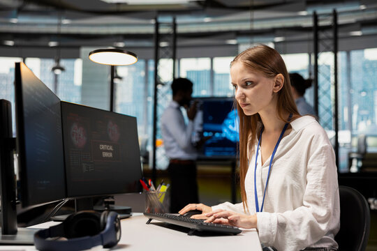 Worried young female programmer debugging code in office, looking for solutions to fix errors on screen. Frowning intern reviewing error logs at PC, trying to to resolve critical glitches