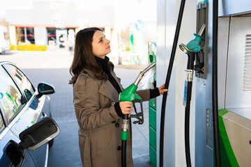 Woman looking at fuel pump display while refueling car at gas station