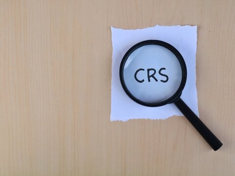 Magnifying glass over crs text on white paper on wooden background with copy space. Business concept 