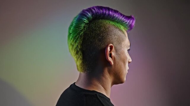 Man with vibrant multicolored mohawk hairstyle poses in front of a softly lit background, showcasing hair color transitions and unique style