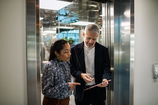 Diverse coworkers reviewing tablet in modern office elevator