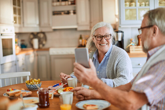 Happy senior couple using smartphone during breakfast at home kitchen