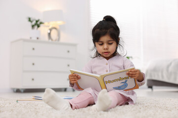 Naklejka premium Cute little girl reading book on floor at home. Space for text
