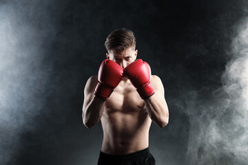 Athletic man in red boxing gloves in smoke against black background