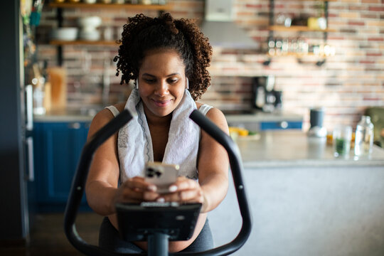 Woman on exercise bike using smartphone in home kitchen