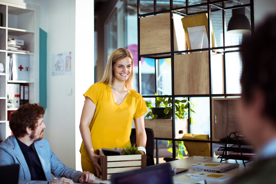 Smiling woman carrying box on first day in modern office
