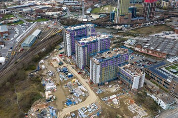Naklejka premium Drone aerial view of residential tower construction site in Holbeck Leeds with cranes railway tracks building materials and surrounding industrial buildings beneath cloudy sky during daytime