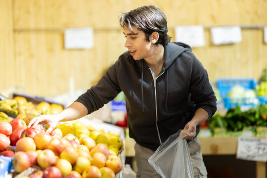 Man chooses ripe apples for purchase in greengrocer shop