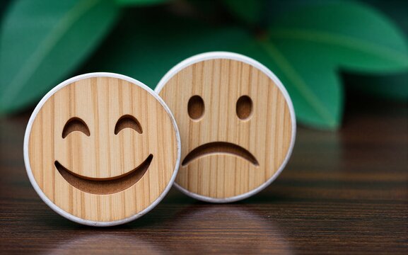 Wooden smiley and frowny faces on a table with green leaves in the