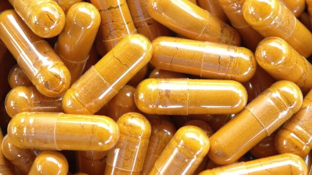 Herbal capsules containing turmeric powder in a wooden bowl. A natural anti-inflammatory dietary supplement.