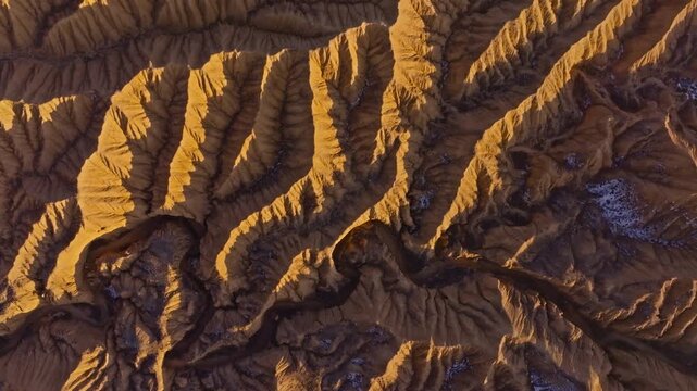 Directly above aerial view of Ak-Say canyons showcases rugged landforms and a winding river. Snow patches contrast with the arid landscape under daylight.