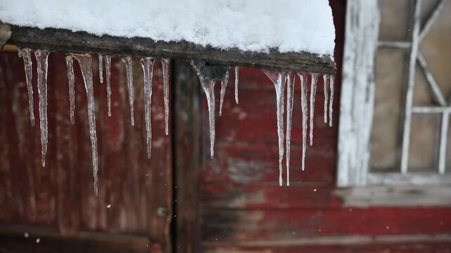 Icicles hanging from a weathered roof ledge over red barn wall
