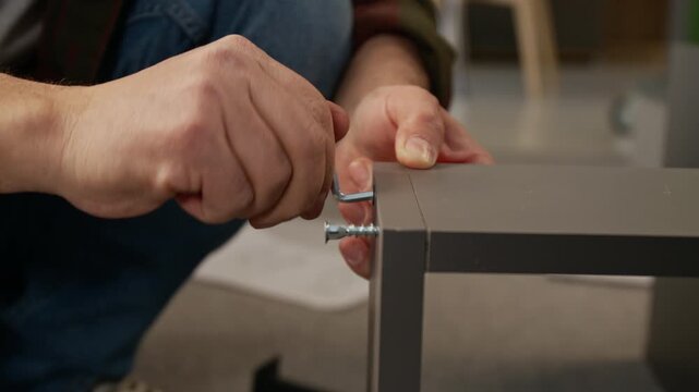 Close-up of hands of unrecognizable man driving in bolts using hex key tool, fixing together panels, while assembling flat pack locker or drawer at home