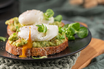 Delicious breakfast of two poached eggs on crusty sourdough bread with smashed guacamole and a...