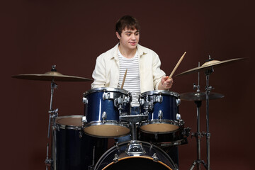 Teenage boy with drumsticks learning how to play drums on brown background