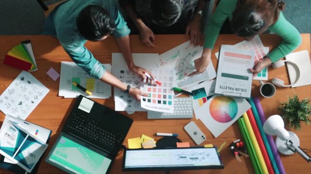 Top down aerial view of project manager looking at screen while designer writing idea. Smart business team explain idea of logo design while designer choose theme while looking at palette. Symposium.
