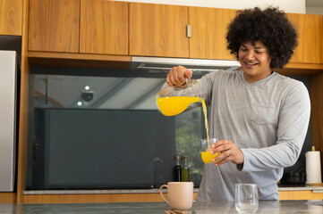 Mid adult African-American in gray shirt pouring OJ from pitcher into glass in kitchen, copy space © wavebreak3