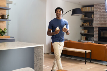 Naklejka premium African American man walking through open-plan home holding two beverage bottles near marble island