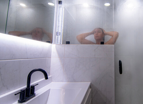 Mujer hispana mexicana tomando una ducha caliente como parte de la higiene personal ba&ntilde;o diario de la cultura de Mexico. ba&ntilde;o con luz blanca y puertas de cristal, ducha caliente, horizontal